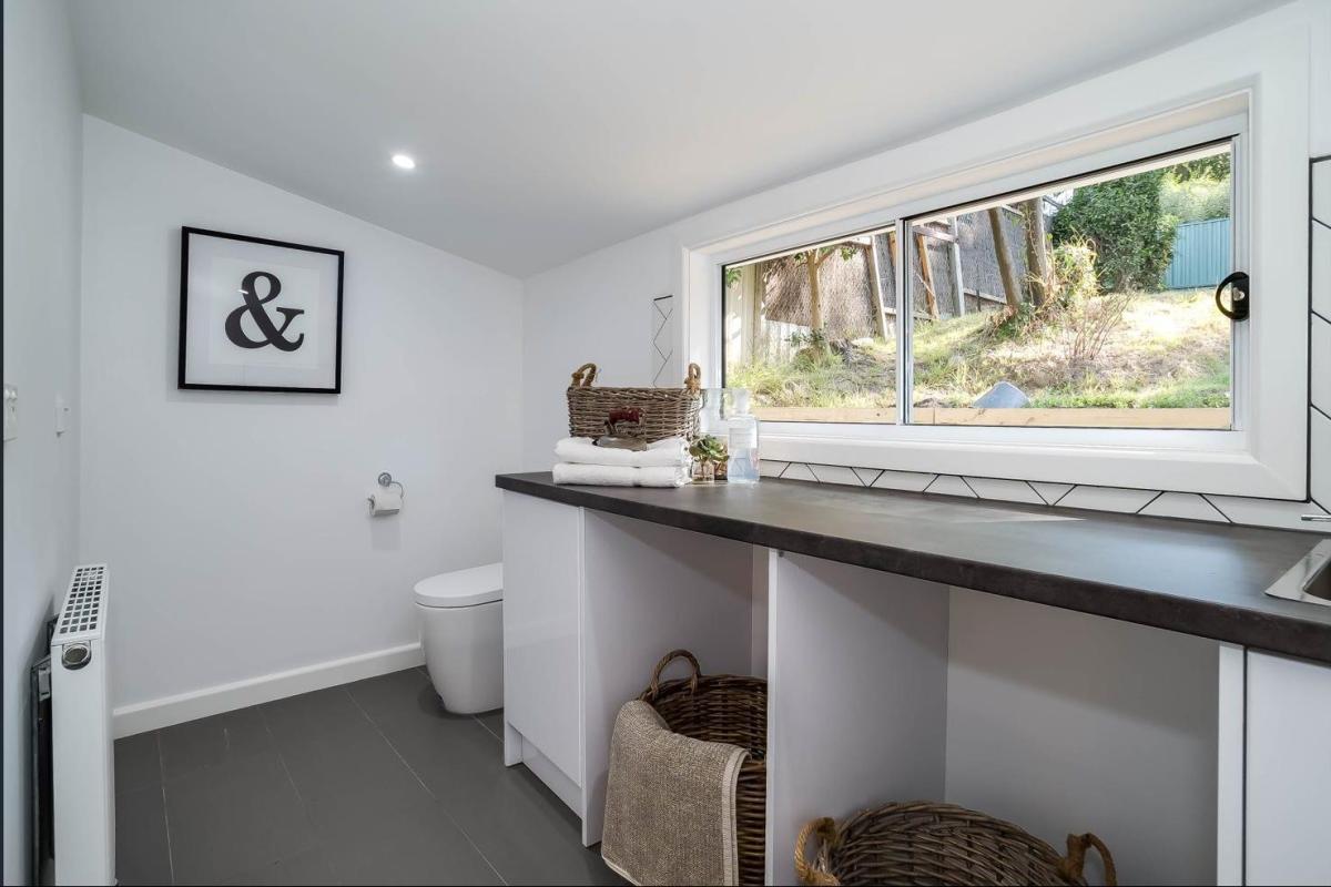 Modern white laundry room with long bench, open shelving, sink and window