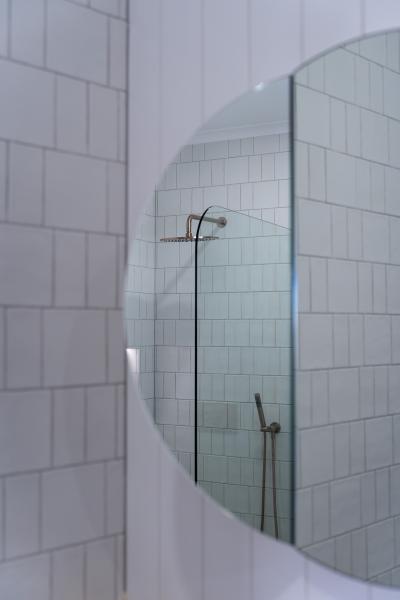 Round mirror reflecting a tiled shower with chrome tapware in a modern white bathroom