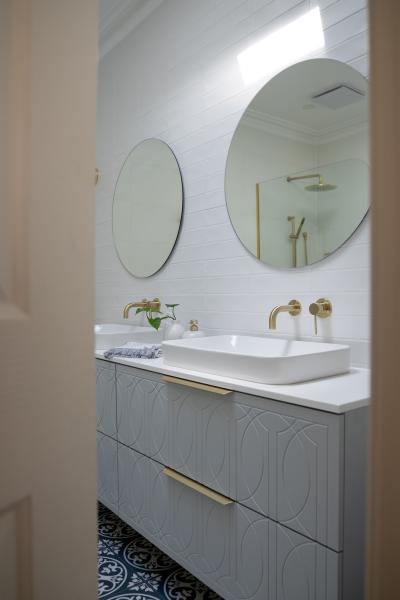 Modern white bathroom vanity with round mirrors and brushed brass tapware