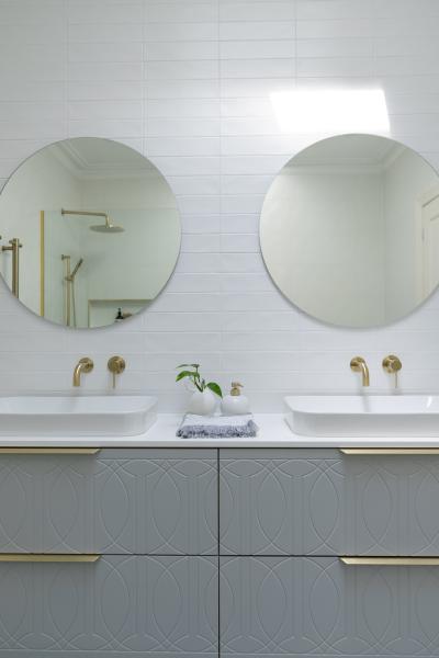 Modern double vanity bathroom with two round mirrors, white basins and brushed brass tapware