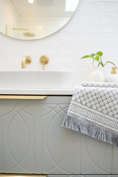 White bathroom vanity with brass tapware, round mirror and textured hand towel