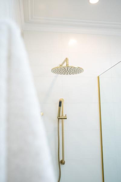 Brushed brass shower set with round rain head in a modern white tiled bathroom