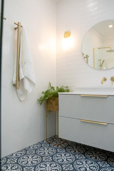Modern bathroom vanity with brass handles, round mirror and patterned floor tiles