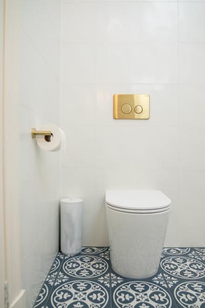 Modern wall-hung toilet with brass flush plate and patterned floor tiles