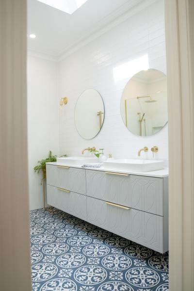 Bright bathroom with double vanity, round mirrors and patterned floor tiles