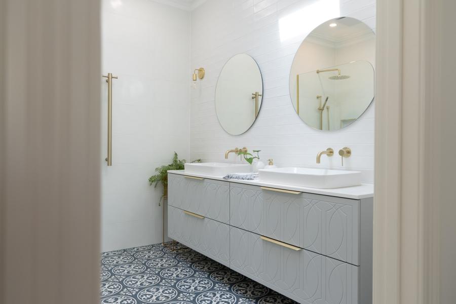 Modern white bathroom with double vanity, round mirrors and patterned floor tiles