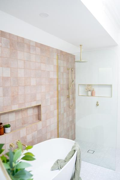 Modern bathroom with curved freestanding bath, pink tiled feature wall and brass shower fittings