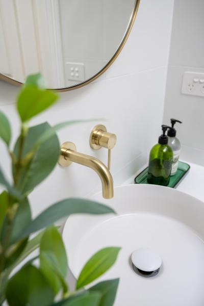 Brass wall-mounted tap above a white basin in a modern bathroom vanity