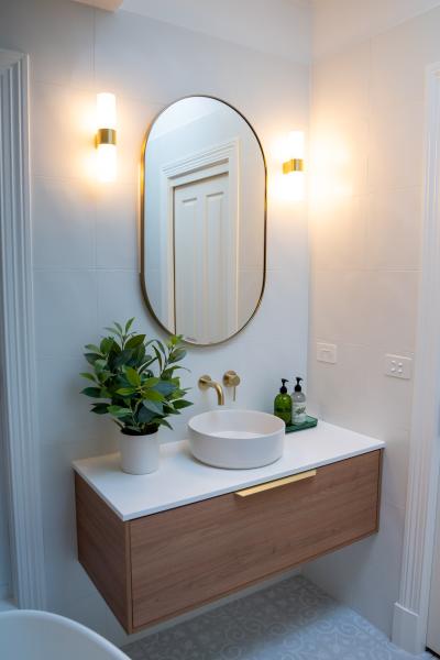 Floating timber vanity with round basin, oval mirror and wall lights in a modern bathroom