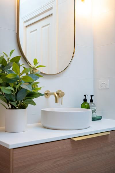 Modern bathroom vanity with vessel basin, oval mirror, brass tapware and indoor plant
