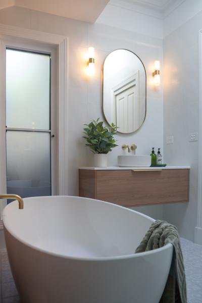 Freestanding bath beside floating timber vanity and oval mirror in a modern white bathroom