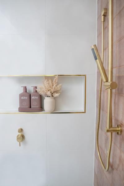 White tiled shower niche with blush bottles and brushed brass shower rail and mixer