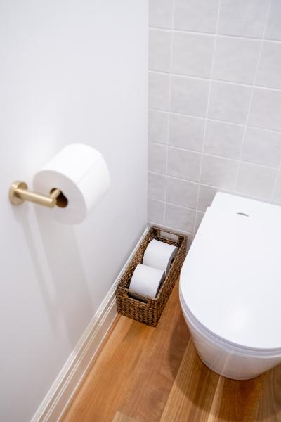 Modern bathroom toilet with brass toilet roll holder, spare roll basket and light tiled wall