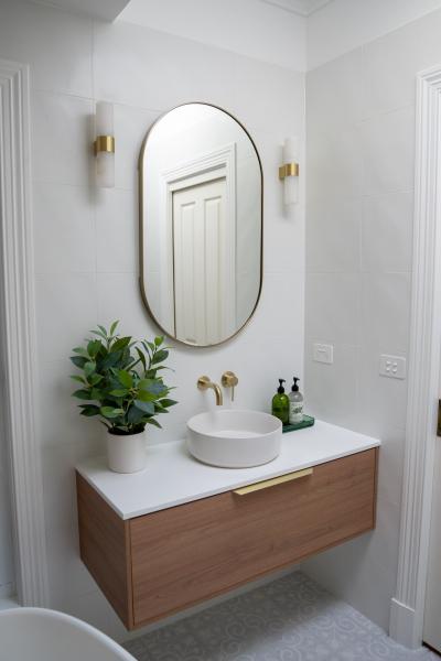 Wall-mounted timber vanity with round basin and arched mirror in a modern white bathroom
