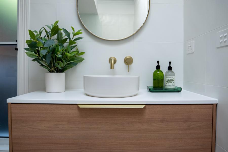 Modern timber vanity with round basin, wall taps and mirror in a bright white bathroom