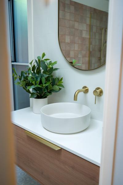 Modern bathroom vanity with round basin, brass wall taps and arched mirror