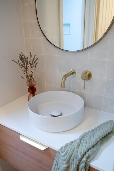 Round white basin on timber vanity with brushed brass tap and mirror in a modern bathroom