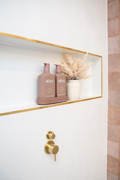 Built-in shower niche with gold trim, toiletry bottles and soft beige tiles
