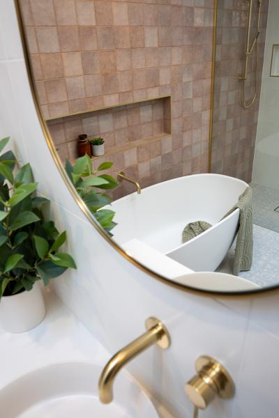 Freestanding bath beside blush pink tiled shower wall with brass tapware and round mirror