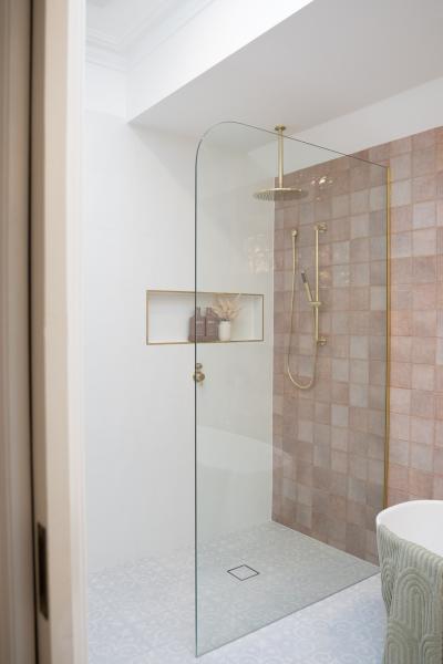 Walk-in shower with blush pink tiles, brass fittings and recessed niche in a modern bathroom