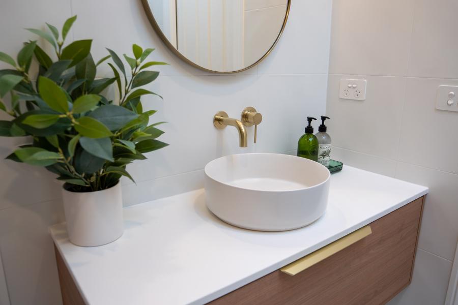 Modern bathroom vanity with round basin, brass wall taps and potted plant