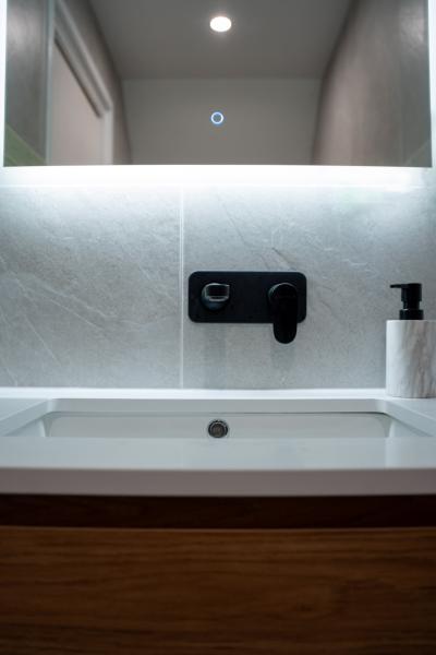 Modern bathroom vanity with white basin, black wall-mounted tapware and illuminated mirror