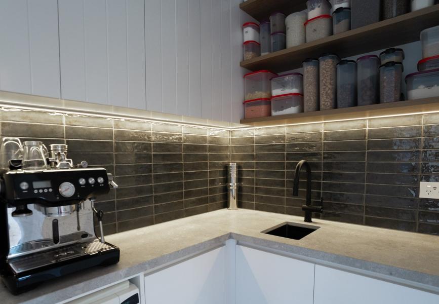 Modern kitchenette with white cabinetry, dark tiled splashback, coffee machine and under-shelf lighting