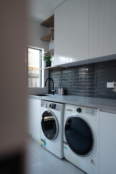 Modern white laundry with front-loading washer and dryer, grey splashback and tall cabinetry