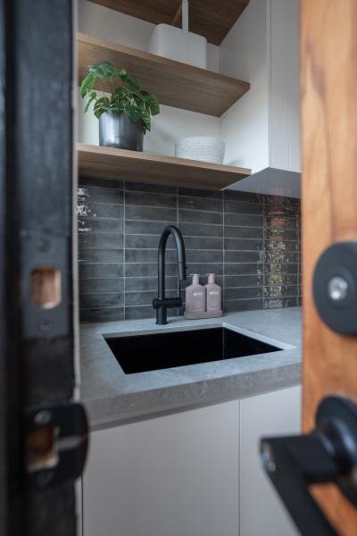 Compact laundry with black sink, grey tiled splashback and timber open shelves