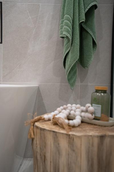 Timber stool beside a white bath with green towel and bathroom accessories