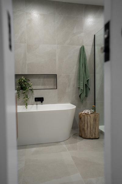Modern bathroom with freestanding bath, tiled walls, recessed shelf and green towel