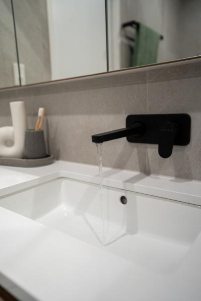 Matte black wall-mounted bathroom tap over a white basin with mirror and accessories