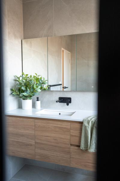 Modern bathroom vanity with timber cabinetry, black tapware, mirror and potted plant