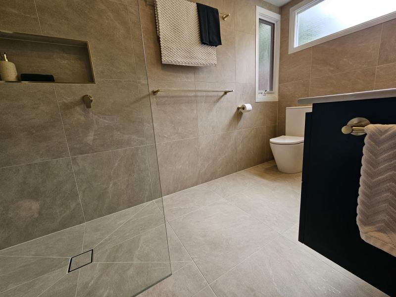 Modern beige tiled bathroom with walk-in shower, niche shelf and wall-hung toilet