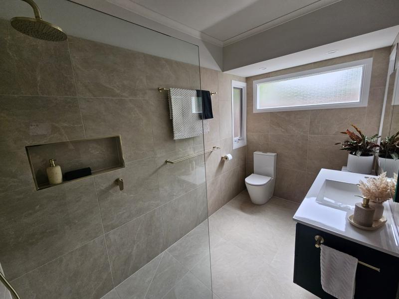 Modern bathroom with walk-in shower, niche shelving, toilet and vanity in neutral stone-look tiles