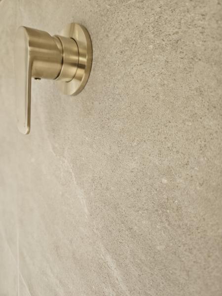 Brushed brass shower mixer mounted on a textured beige tiled bathroom wall