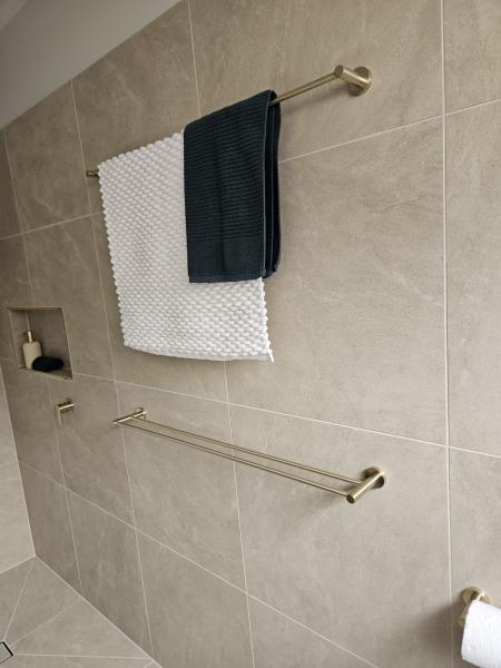 Two towel rails on a beige tiled bathroom wall with folded white and dark towels