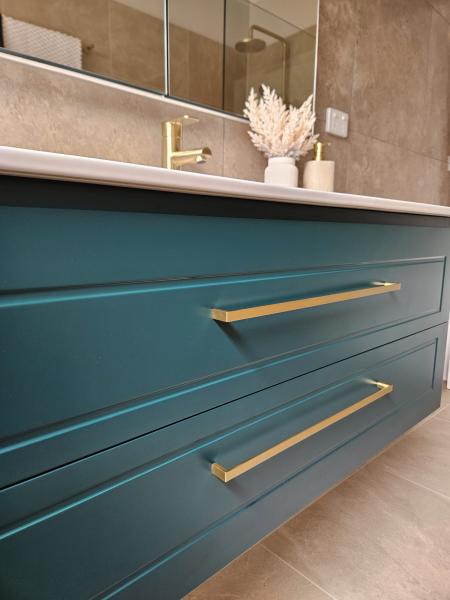 Teal floating bathroom vanity with brass handles beneath mirrored wall cabinet