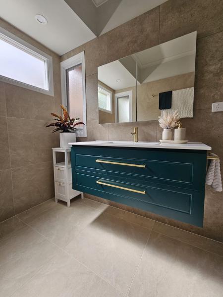 Modern bathroom vanity with teal cabinetry, brass tapware and beige wall tiles