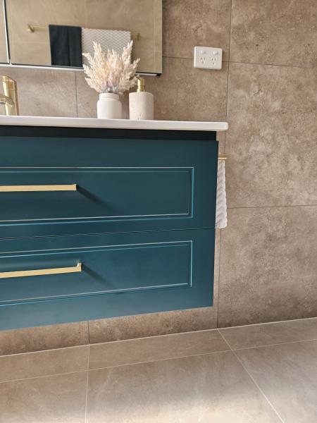 Floating teal bathroom vanity with brass handles against large stone-look wall tiles