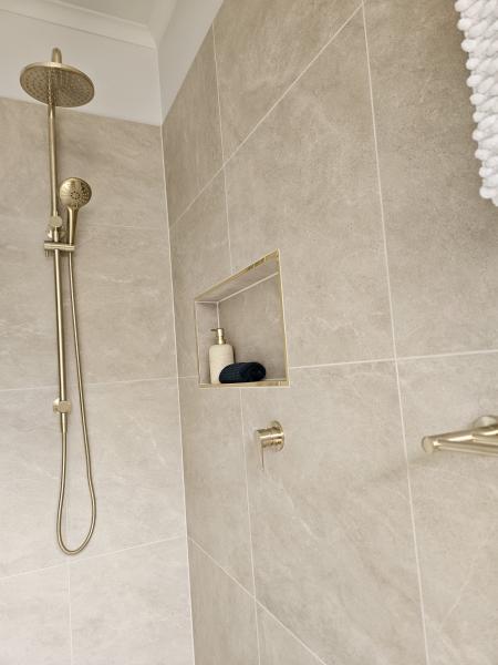 Walk-in shower with brushed brass fittings and recessed niche in beige tiled bathroom
