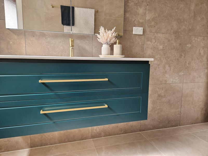 Floating teal bathroom vanity with brass handles against beige tiled walls and floor
