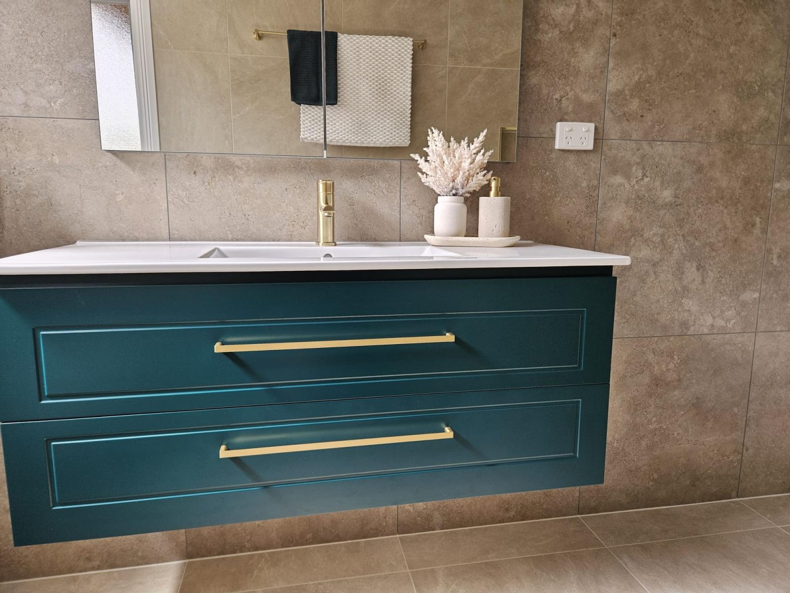 Teal floating bathroom vanity with brass handles against beige tiled wall