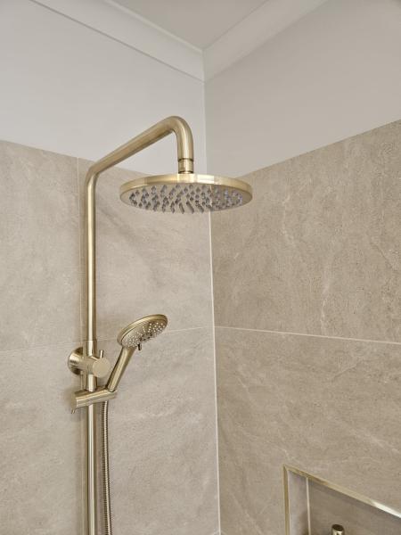 Brushed brass rain shower and handheld shower on beige tiled bathroom wall