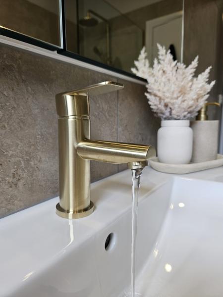 Brushed brass bathroom tap over a white ceramic basin in a modern vanity setting