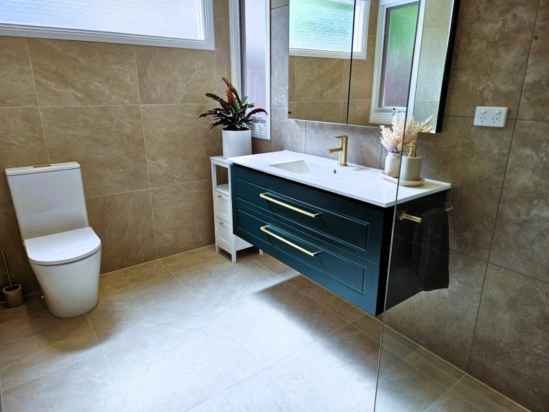 Modern bathroom with floating navy vanity, wall mirror, beige tiles and toilet