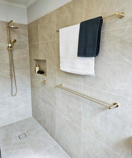Walk-in tiled shower with brushed brass fixtures and towel rails