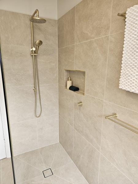 Walk-in shower with beige tiles, brushed brass fittings and recessed niche