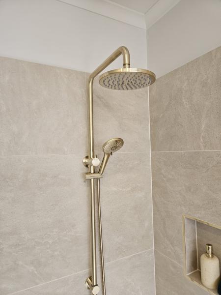 Brushed brass shower set on light stone-look tiled bathroom wall