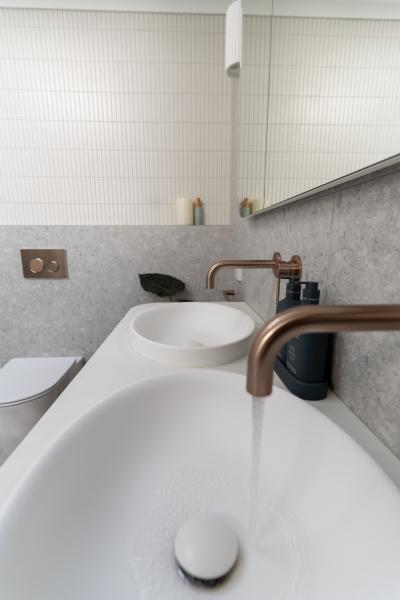 Modern bathroom vanity with white basin, brushed brass tapware and textured wall tiles